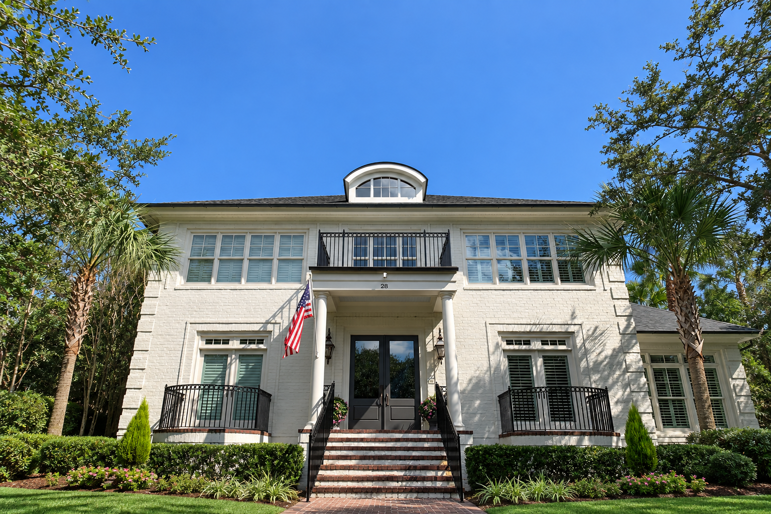 White brick home with black railings, front steps, and an American flag beneath a blue sky